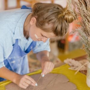 Focused woman creating handmade clay art with natural materials indoors.