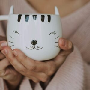 A woman holds a ceramic mug with a cute cat face design, perfect for cozy indoors setups.