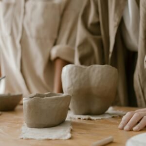 Artisan hands crafting pottery bowls on a wooden table indoors, showcasing traditional clay art.