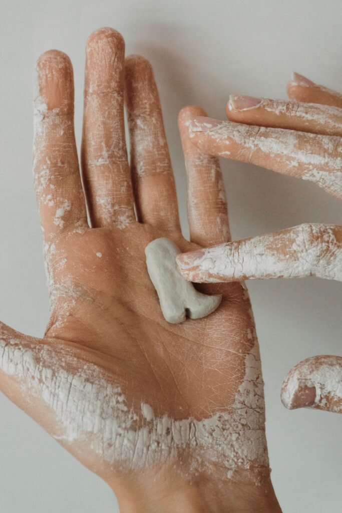 Detailed close-up of hands applying white clay on skin, showing texture and detail.