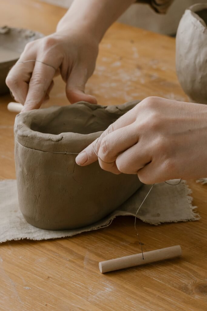 Close-up of hands shaping clay pottery with sculpting tools in a workshop.