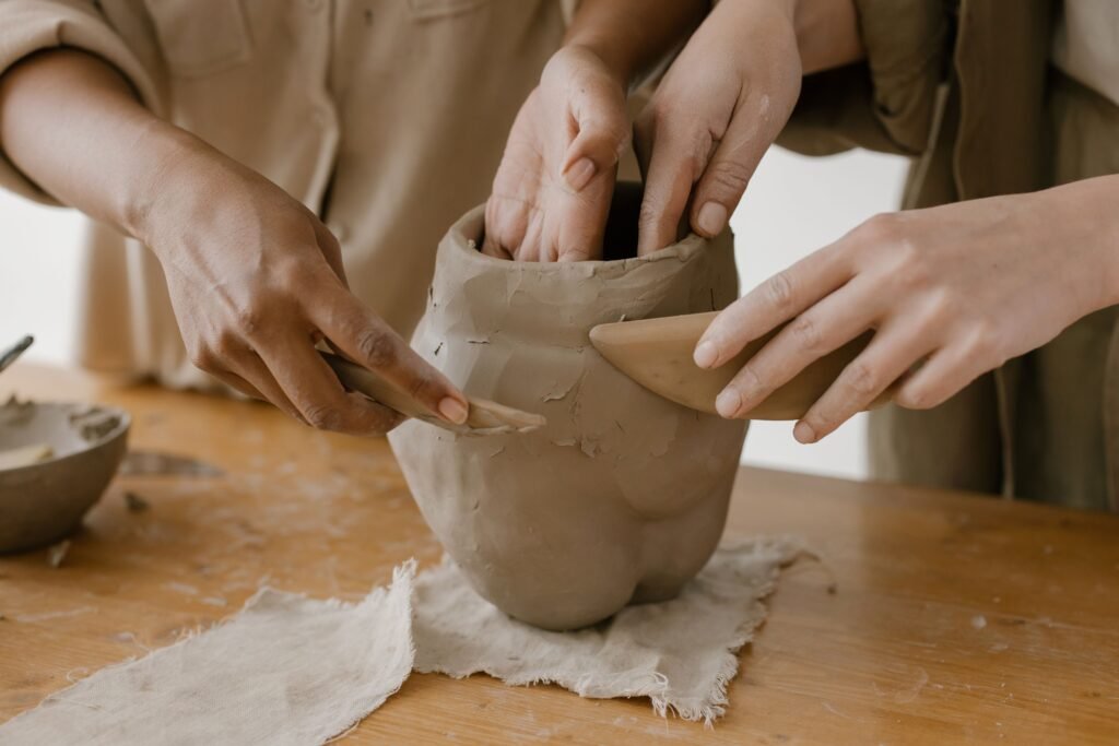 Hands shaping clay pottery collaboratively, showing craftsmanship.