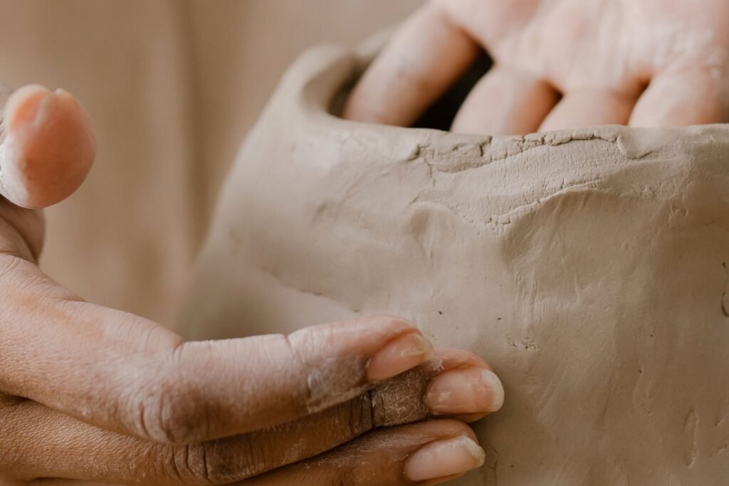 Close-up of hands shaping clay in pottery workshop, showcasing artisanal craft details.