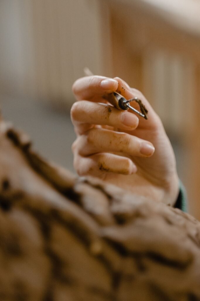 Detailed view of a hand working on a clay sculpture using a loop tool, emphasizing artisanal craftsmanship.